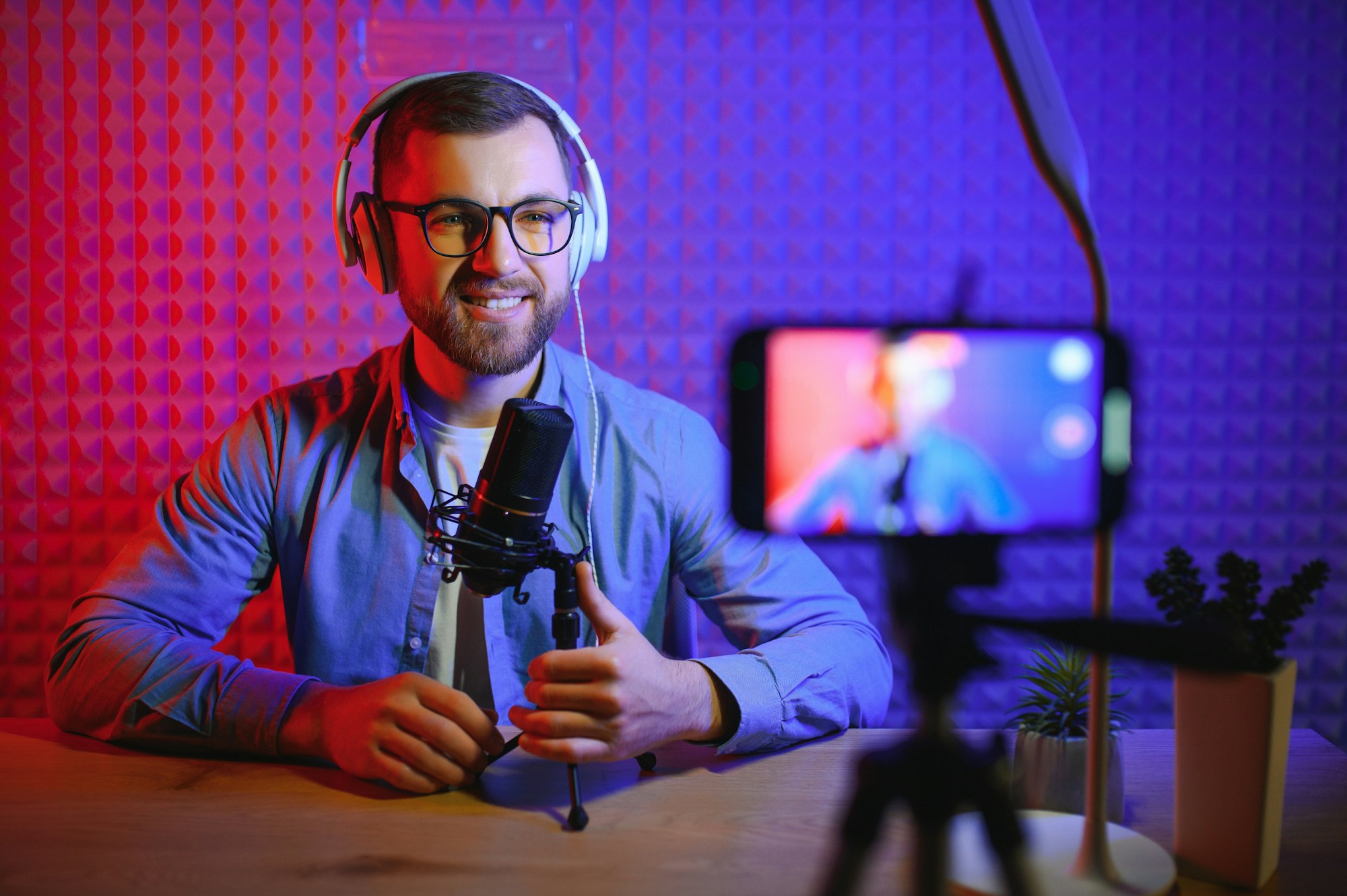 Young man recording or streaming podcast using microphone at his small broadcast studio.